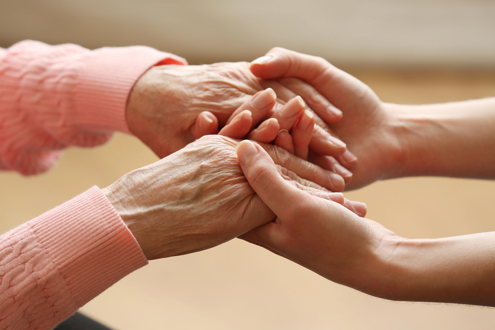 An adult's hand grasps an older, sun-wrinkled hand with care
